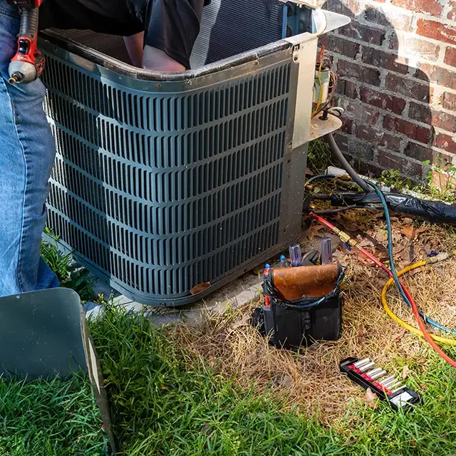 Lincoln Heating & Air repair technician repair an older AC condenser unit outside a brick home in Springfield, IL