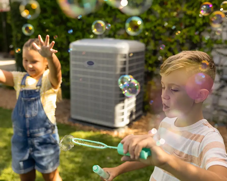 Children blowing bubbles in backyard near a quiet Carrier AC unit serviced by Lincoln Heating & Air in Springfield, IL