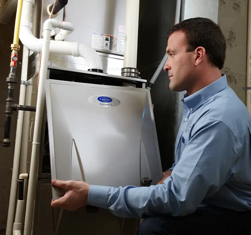 Lincoln Heating & Air technician examining a Carrier Infinity gas furnace in a home basement in Springfield, IL