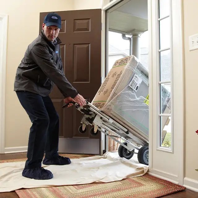 Lincoln Heating & Air delivery technician wheeling in a new Carrier furnace unit for installation in a Springfield, IL home