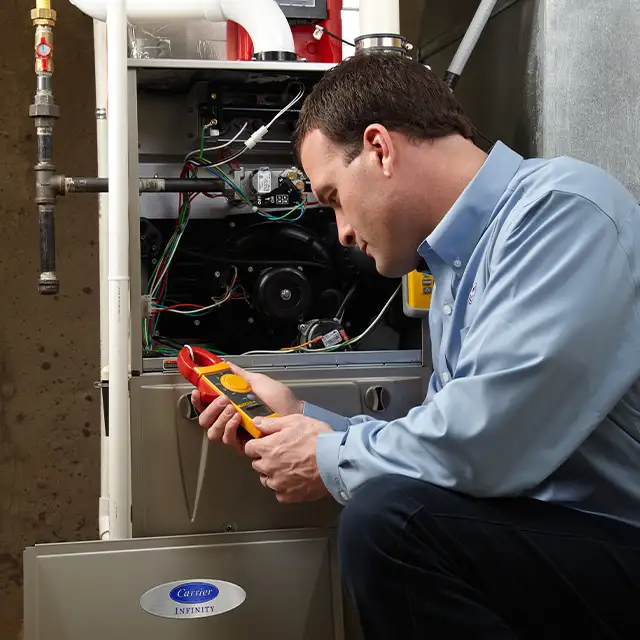 Lincoln Heating & Air technician using a clamp meter to diagnose Carrier furnace electrical components in Springfield, IL