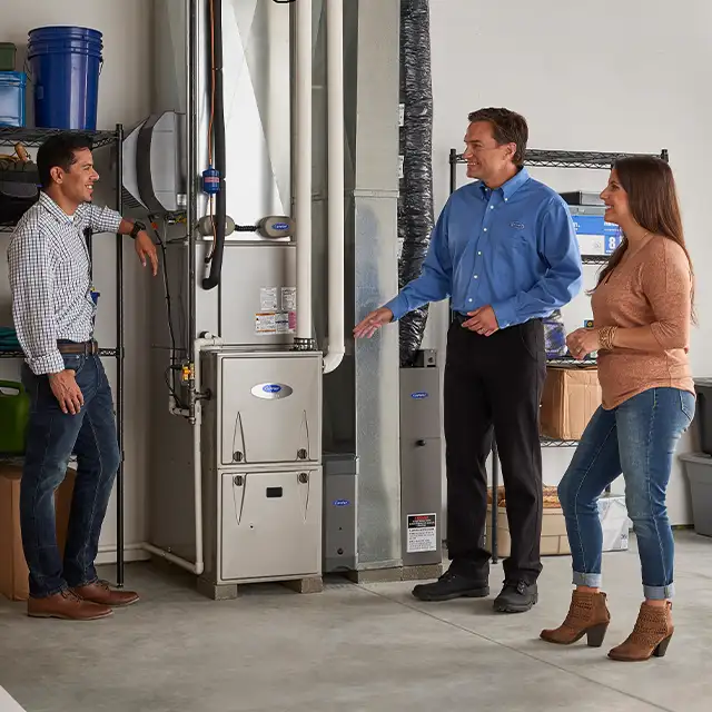 Homeowners consulting with a Lincoln Heating & Air technician beside their Carrier furnace in a Springfield, IL garage