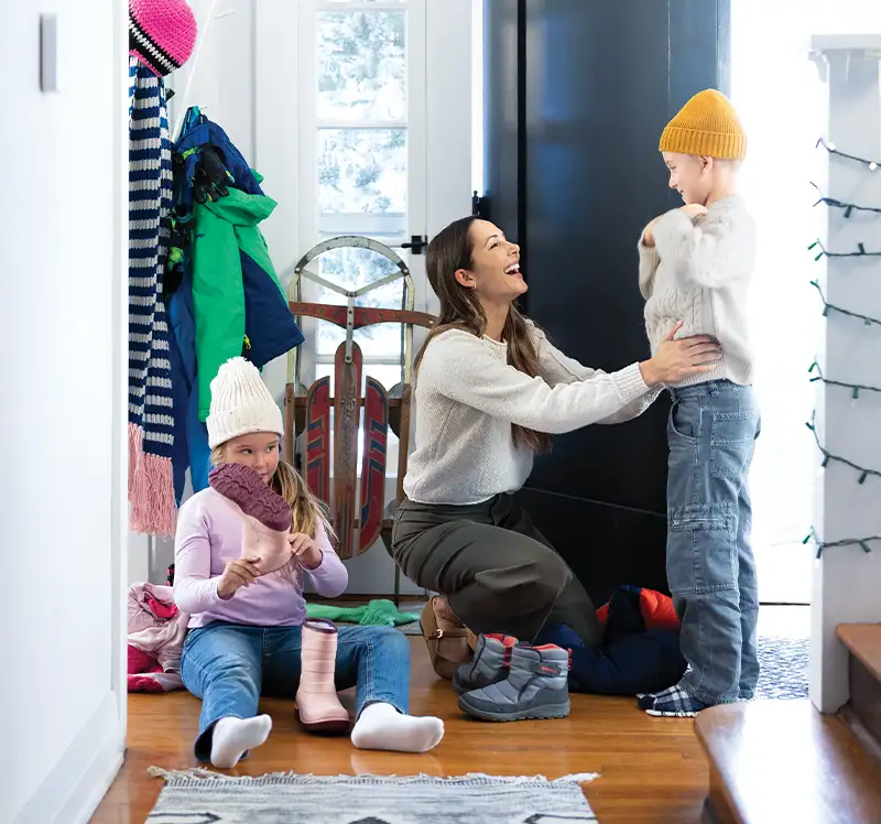 Mother helping kids into winter boots and coats in a warm, comfortable home heated by Lincoln Heating & Air in Springfield, IL