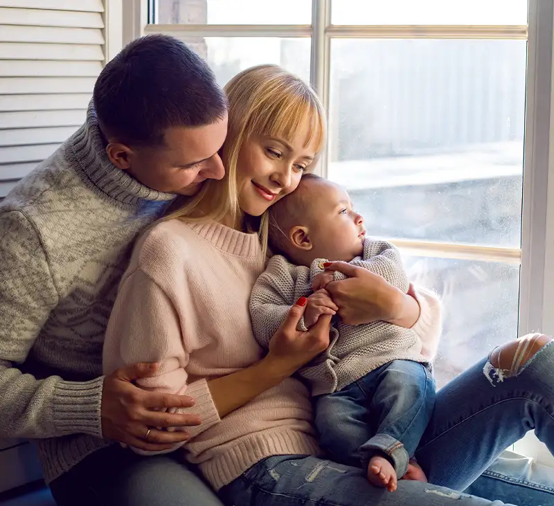Parents cuddling a baby by a bright window in a warm, well-heated, clean, healthy home — Lincoln Heating & Air, Springfield, IL